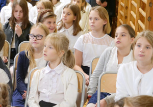 Uczniowie w sali gimnastycznej oglądają w sali gimnastycznej wystąpienie swoich kolegów z okazji Dnia Edukacji Narodowej.