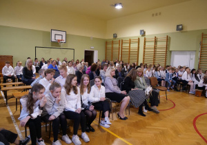 Uczniowie w sali gimnastycznej oglądają w sali gimnastycznej wystąpienie swoich kolegów z okazji Dnia Edukacji Narodowej.