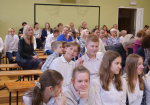 Uczniowie w sali gimnastycznej oglądają w sali gimnastycznej wystąpienie swoich kolegów z okazji Dnia Edukacji Narodowej.