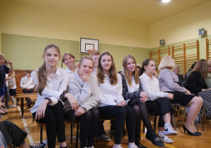 Uczniowie w sali gimnastycznej oglądają w sali gimnastycznej wystąpienie swoich kolegów z okazji Dnia Edukacji Narodowej.
