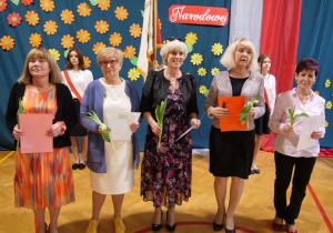 Nagrodzeni nauczyciele za wieloletnią służbę stoją wraz z pamiątkowymi dyplomami.
