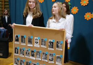Uczniowie klas ósmych stoją z tablicą korkową, na której są zdjęcia nauczycieli z lat dzieciństwa.