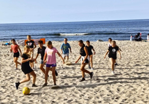 Uczniowie grają na plaży w piłkę nożną.