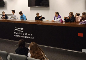 Uczniowie siedzą w sali konferencyjnej.