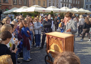 Uczniowie na Starym Mieście słuchają opowieści kataryniarza.