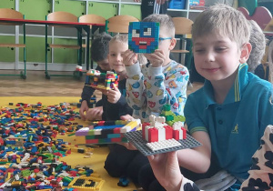 Chłopiec trzyma w ręce wybudowaną przez siebie z klocków Lego budowlę przypominającą twarz.
