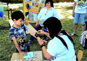 Na zdjęciu stoisko z robieniem tatuaży. Jedna z pań wykonuje chłopcu tatuaż.