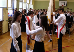 Na zdjęciu uczniowie klas ósmych przekazują sztandar uczniom klas siódmych.