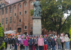 Na zdjęciu uczniowie, którzy stoją przy pomniku Mikołaja Kopernika.