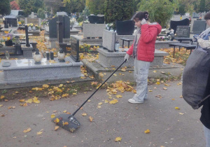 Na zdjęciu uczennica, grabiąca liście na cmentarzu.