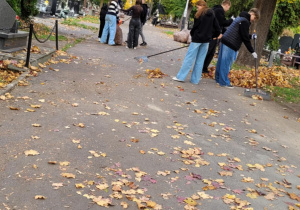 Na zdjęciu uczniowie, grabiący liście na cmentarzu.