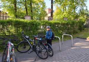 Na zdjęciu chłopiec w kasku rowerowym stoi przy rowerach.