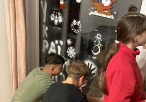 Na zdjęciu uczniowie klasy 7b wraz z dziećmi z domu dziecka dekorują okno.