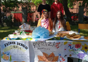 Uczestnicy Pikniku rodzinnego siedzą przy stoisku z potrawami kuchni ukraińskiej.